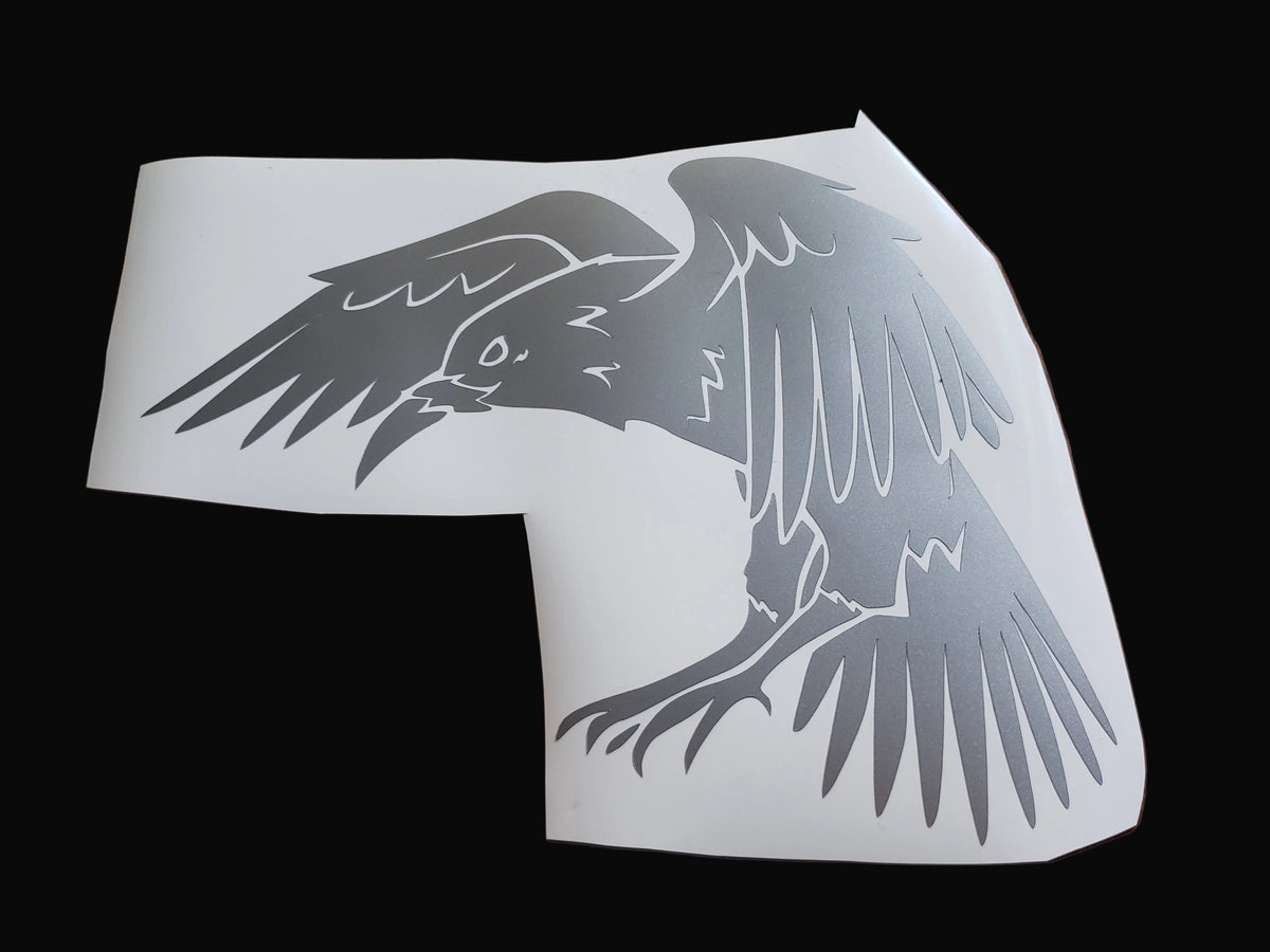 A white vinyl decal sheet featuring a stylized gray raven or crow with wings spread, shown against a solid black background.